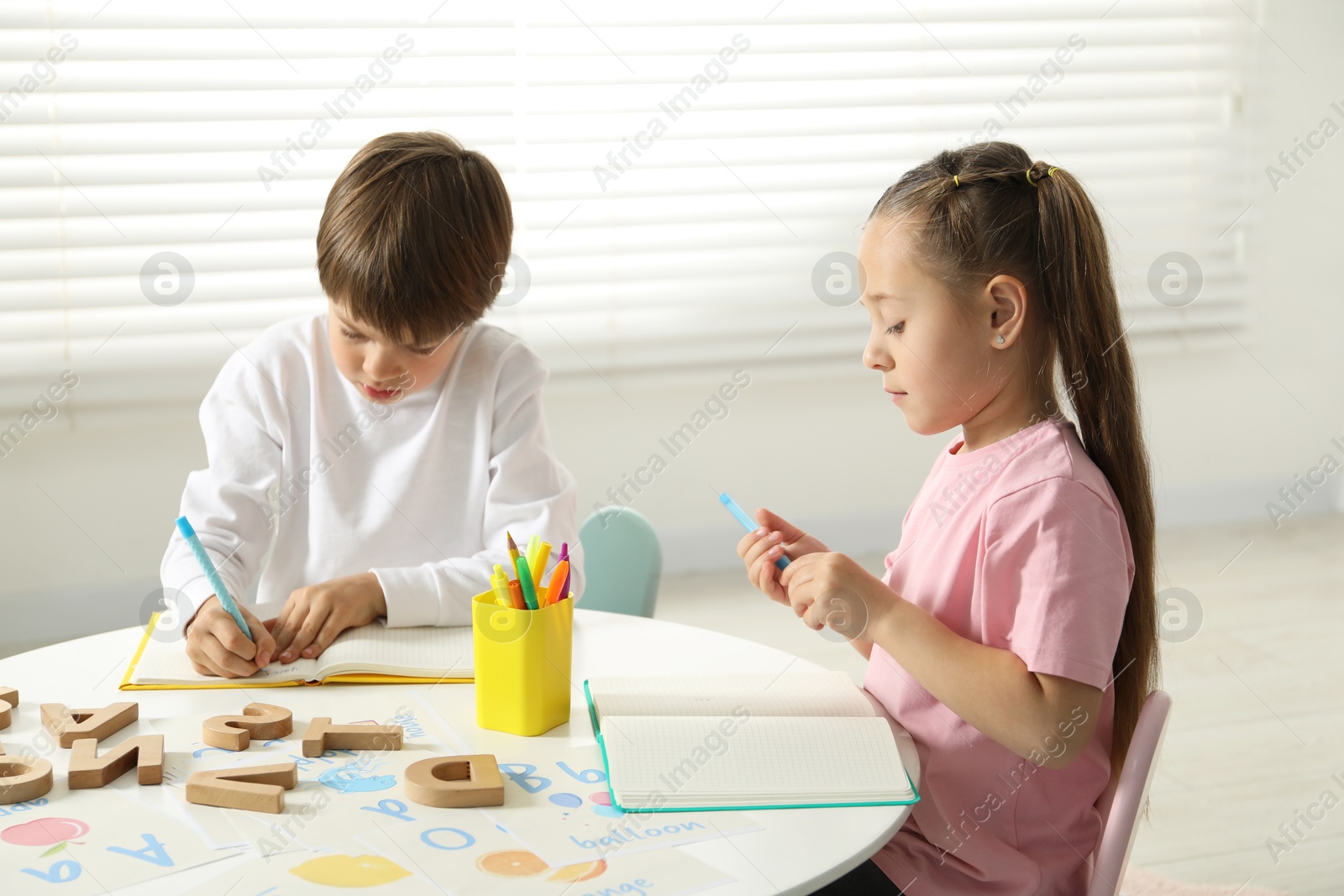 Photo of Little kids learning alphabet at white table indoors