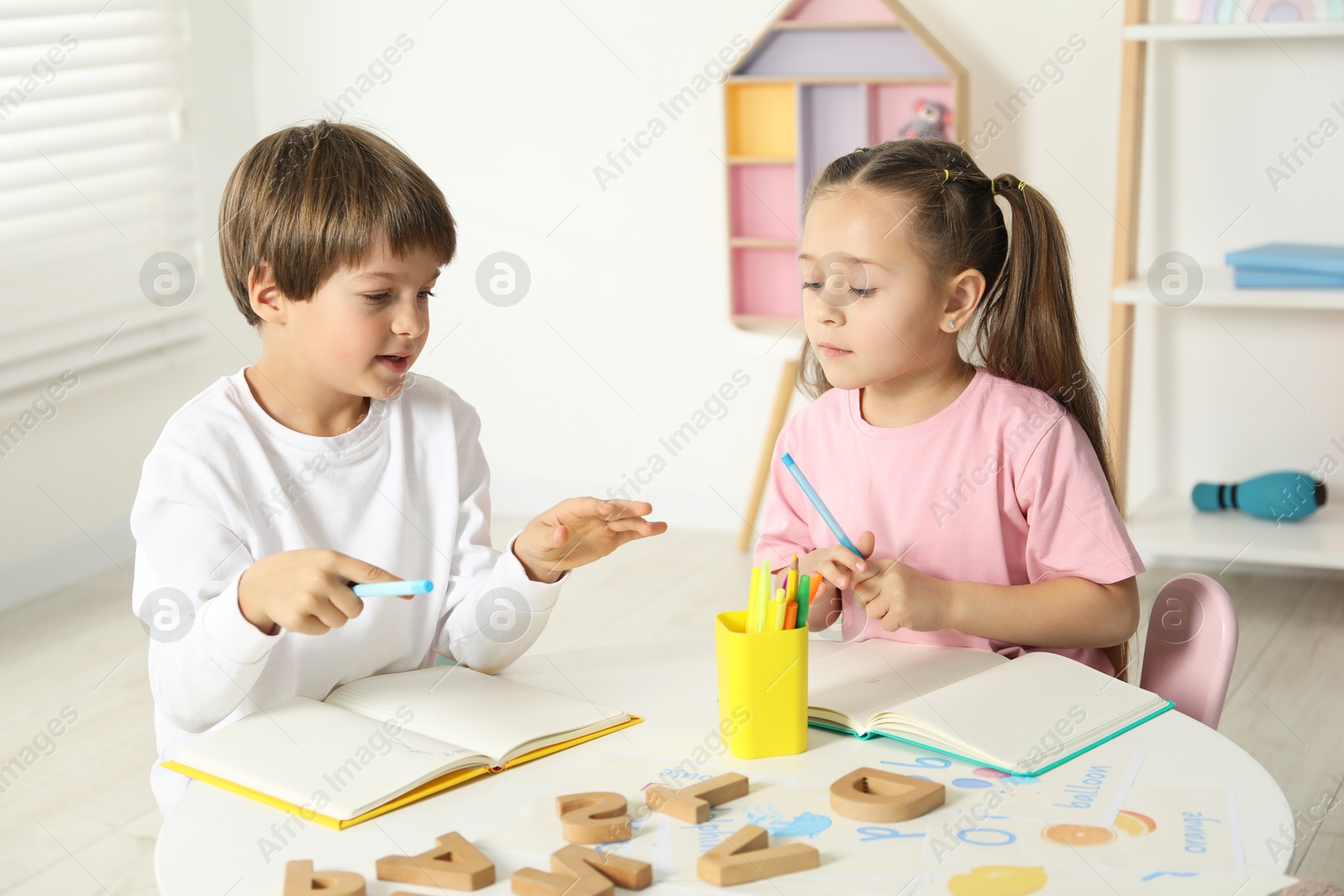 Photo of Little kids learning alphabet at white table indoors