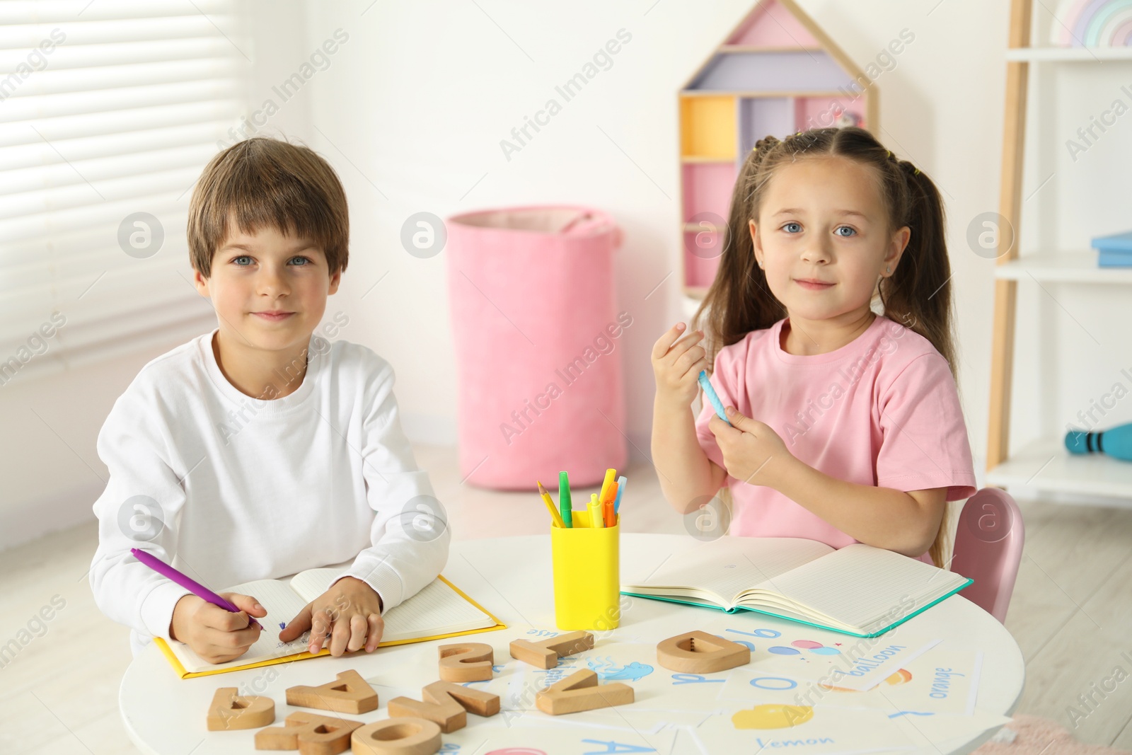 Photo of Little kids learning alphabet at white table indoors