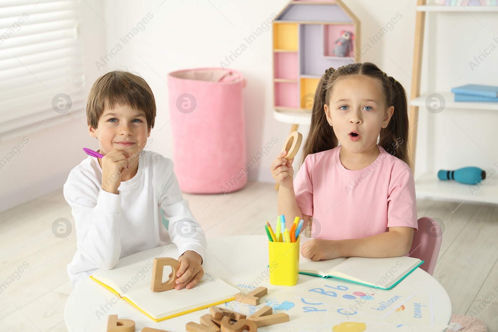 Photo of Little kids learning alphabet with wooden letters at white table indoors