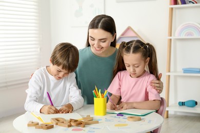 Photo of Speech therapist teaching little kids alphabet at white table indoors