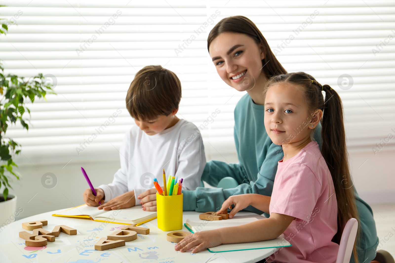 Photo of Speech therapist teaching little kids alphabet at white table indoors