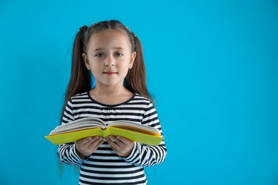 Photo of Learning alphabet. Little girl with book on light blue background, space for text