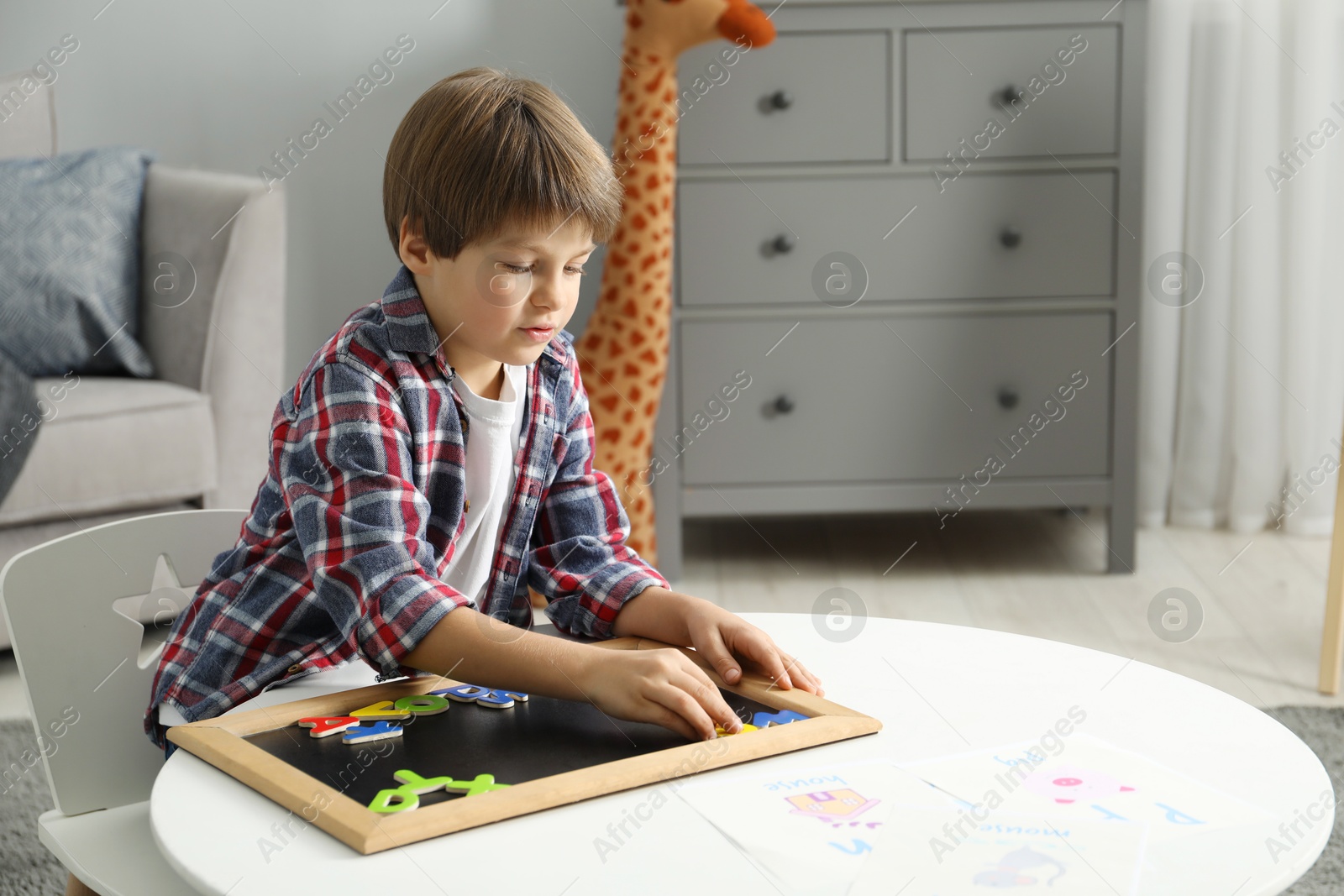 Photo of Little boy learning alphabet with magnetic letters at white table indoors