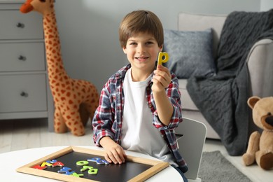 Photo of Little boy learning alphabet with magnetic letters at white table indoors