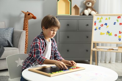 Photo of Little boy learning alphabet with magnetic letters at white table indoors