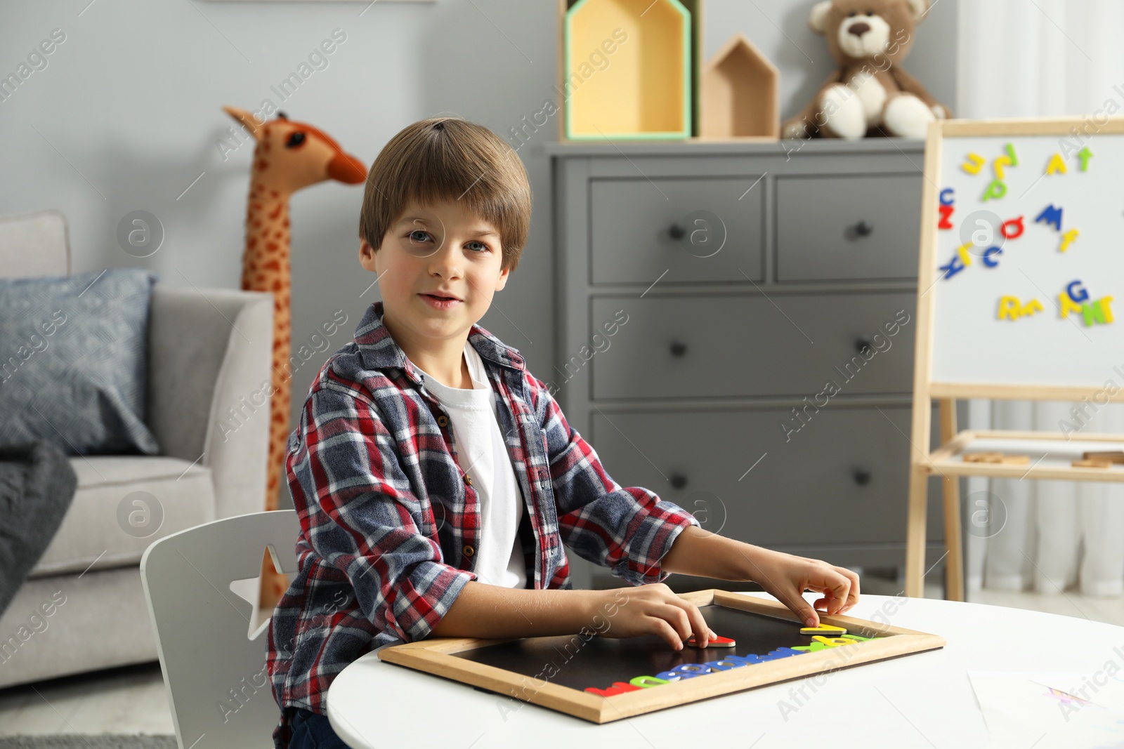 Photo of Little boy learning alphabet with magnetic letters at white table indoors