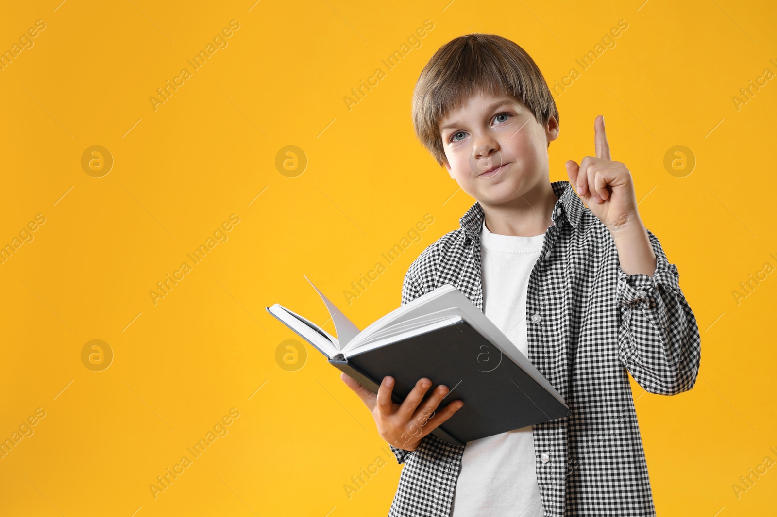 Photo of Learning alphabet. Little boy with book pointing at something on orange background, space for text