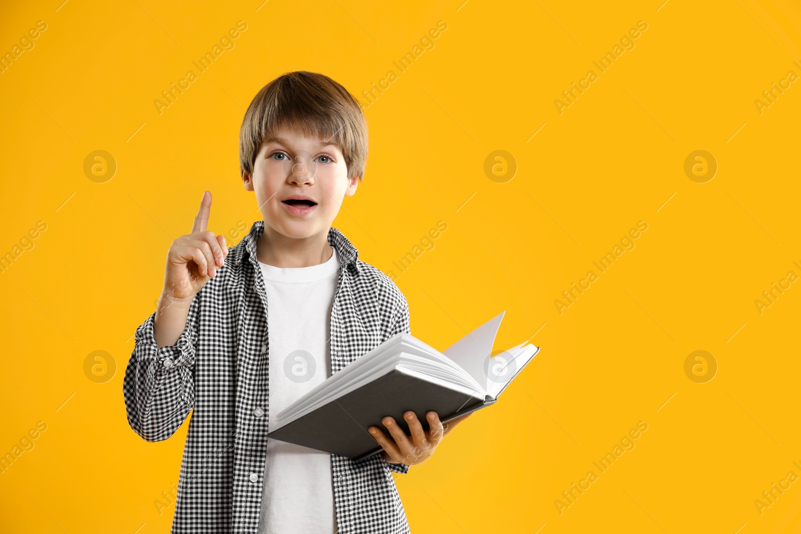 Photo of Learning alphabet. Little boy with book on orange background, space for text