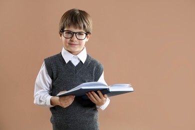 Photo of Learning alphabet. Little boy with book on brown background, space for text