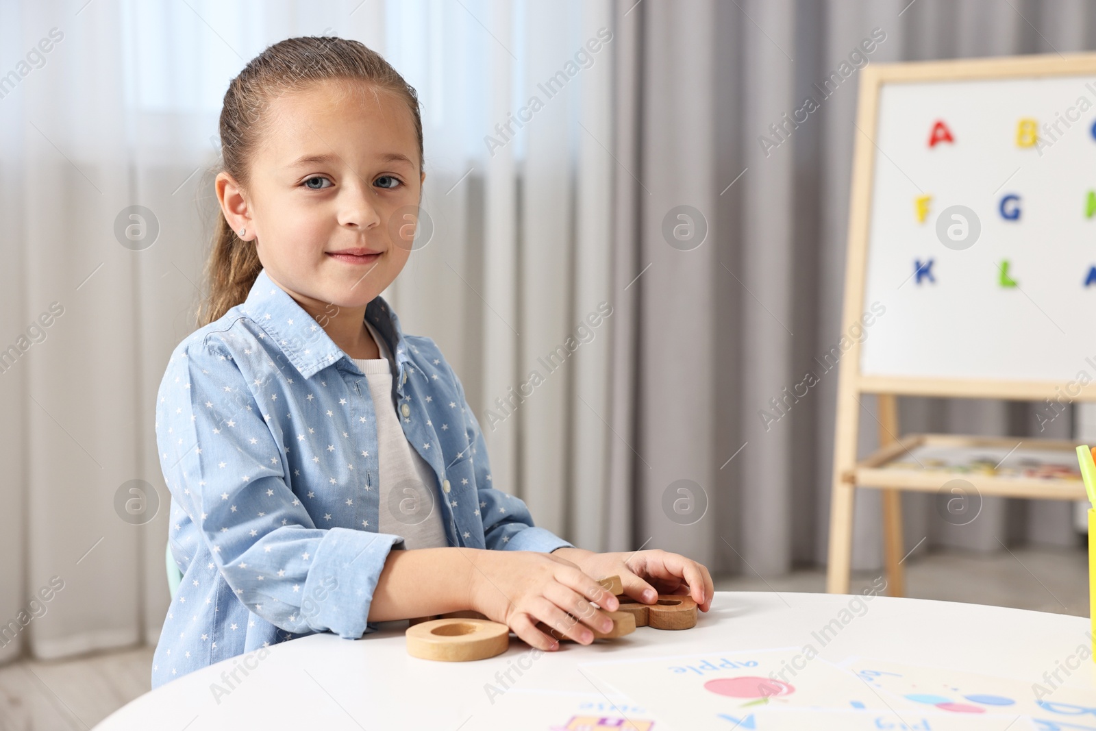 Photo of Little girl learning alphabet with wooden letters at white table indoors