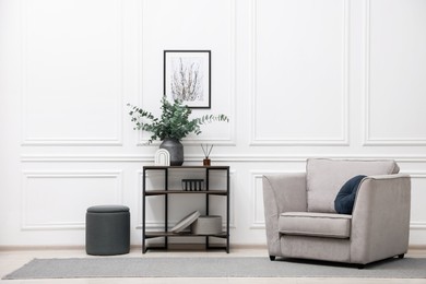 Photo of Console table with decor and armchair near white wall in room. Interior design