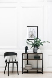 Photo of Console table with decor and chair near white wall in room. Interior design