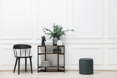 Photo of Console table with decor and chair near white wall in room. Interior design