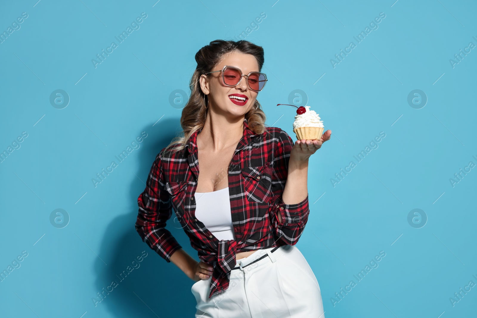 Photo of Happy pin-up woman with cupcake on light blue background