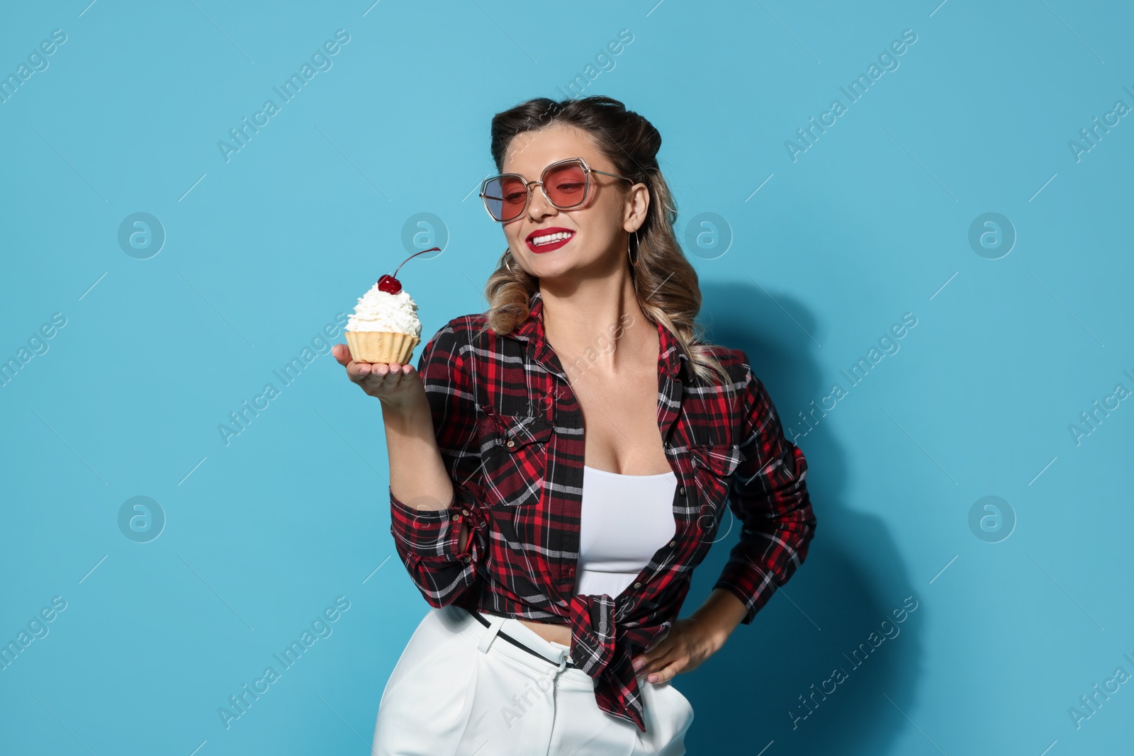 Photo of Happy pin-up woman with cupcake on light blue background