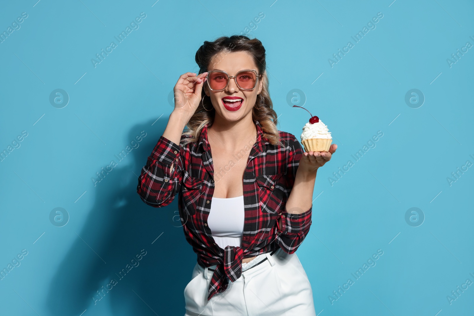 Photo of Happy pin-up woman with cupcake on light blue background