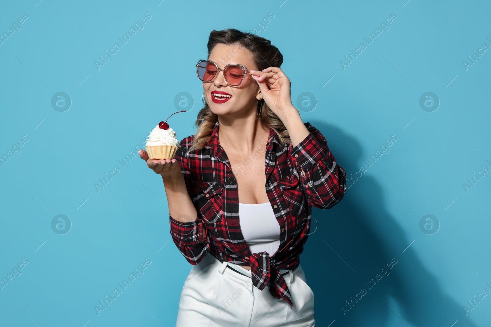 Photo of Happy pin-up woman with cupcake on light blue background