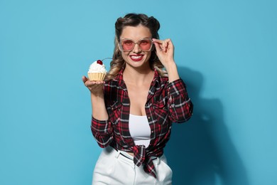 Photo of Happy pin-up woman with cupcake on light blue background