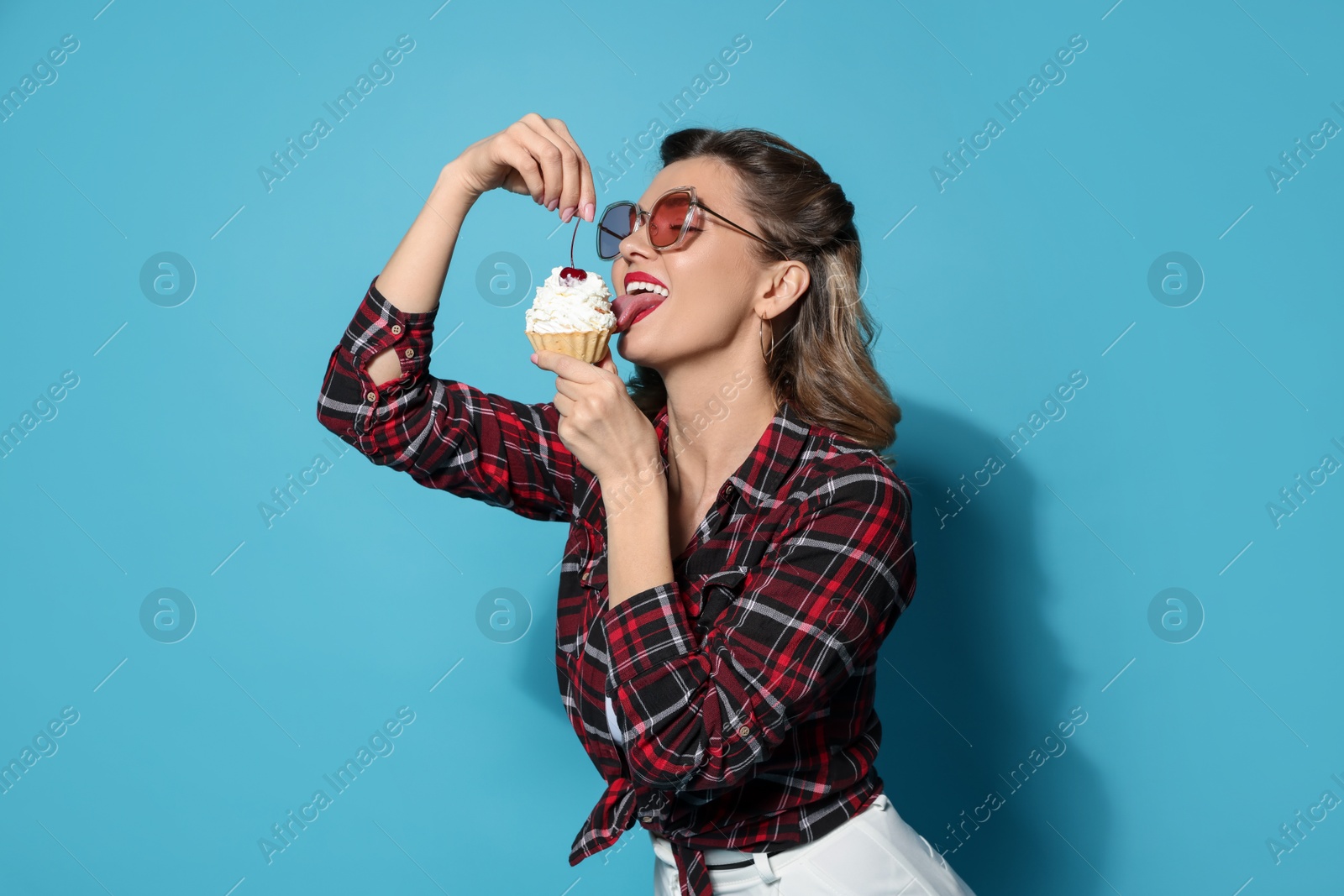 Photo of Attractive pin-up woman eating cupcake on light blue background