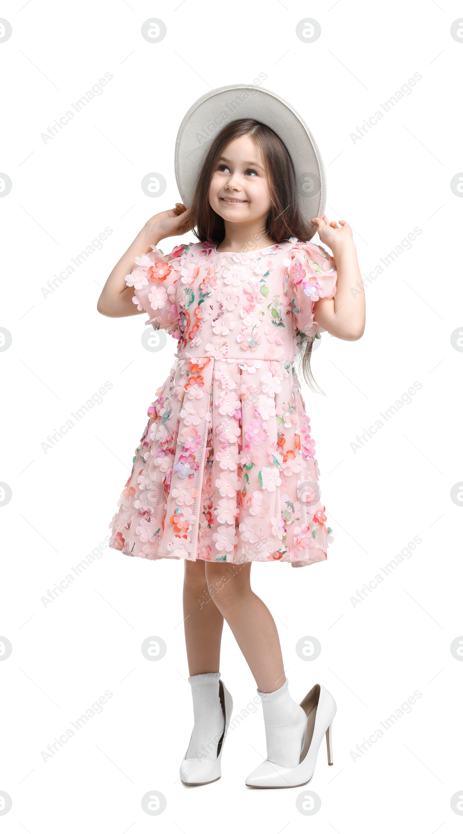 Photo of Stylish little girl wearing oversized high heeled shoes on white background