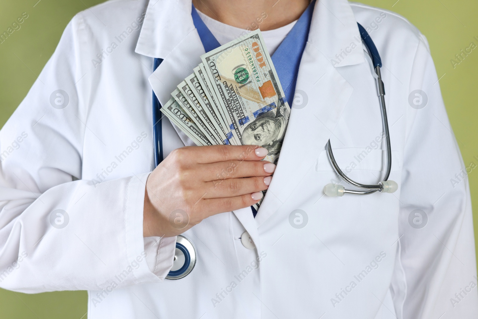 Photo of Corruption concept. Doctor putting dollar banknotes into her coat on green background, closeup