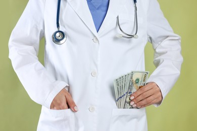 Photo of Corruption concept. Doctor putting dollar banknotes into her pocket on green background, closeup