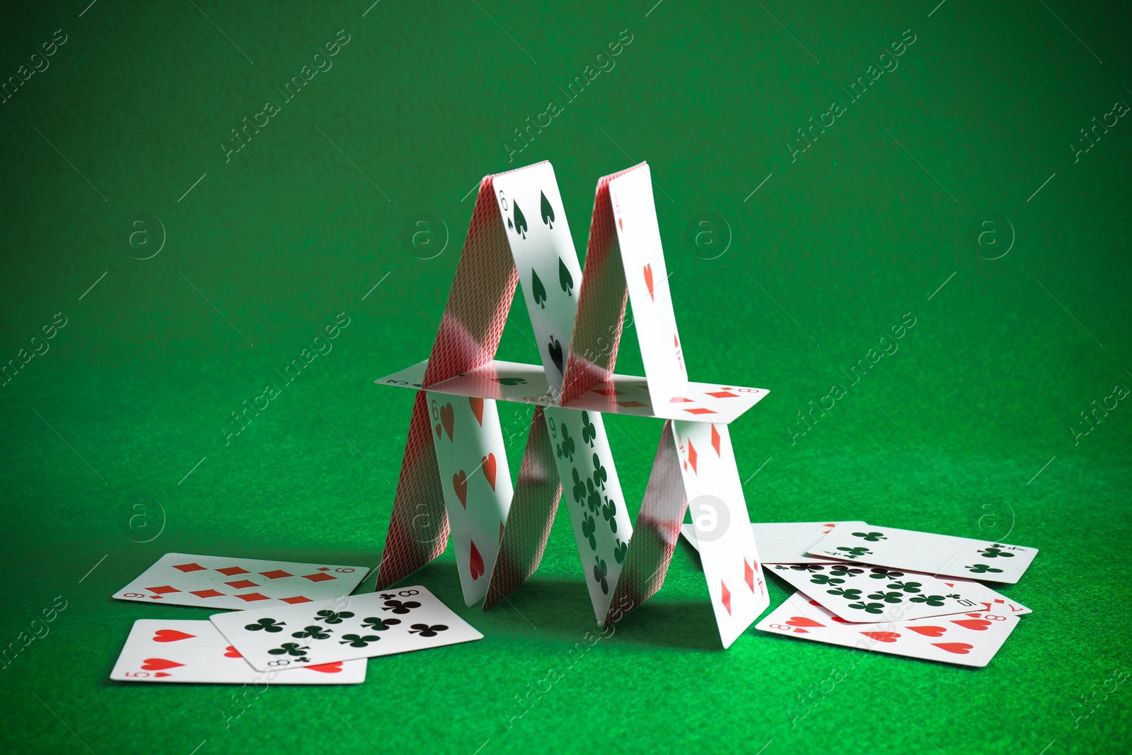 Photo of Collapsed house of playing cards on green background