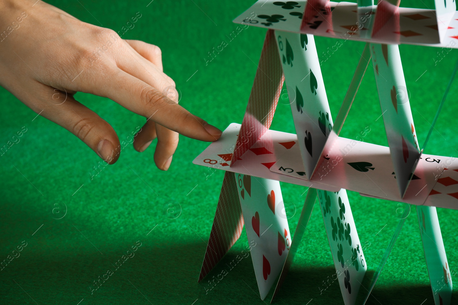 Photo of Woman destroying house of playing cards on green background, closeup