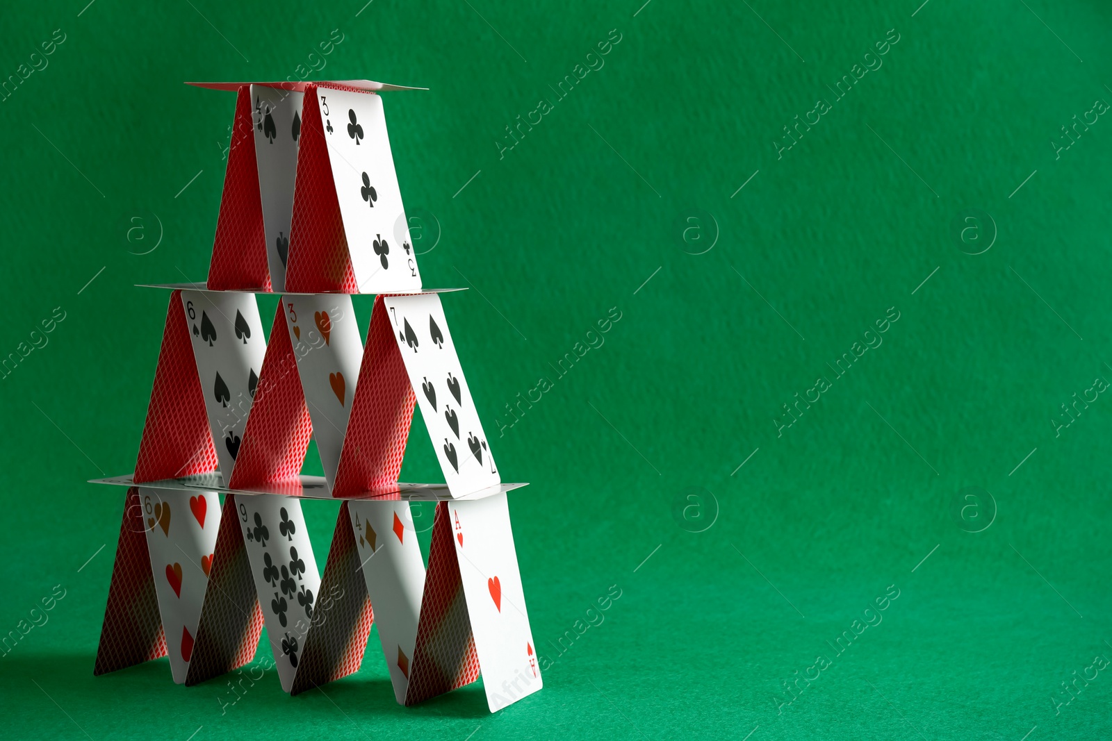 Photo of House of playing cards on green background. Space for text