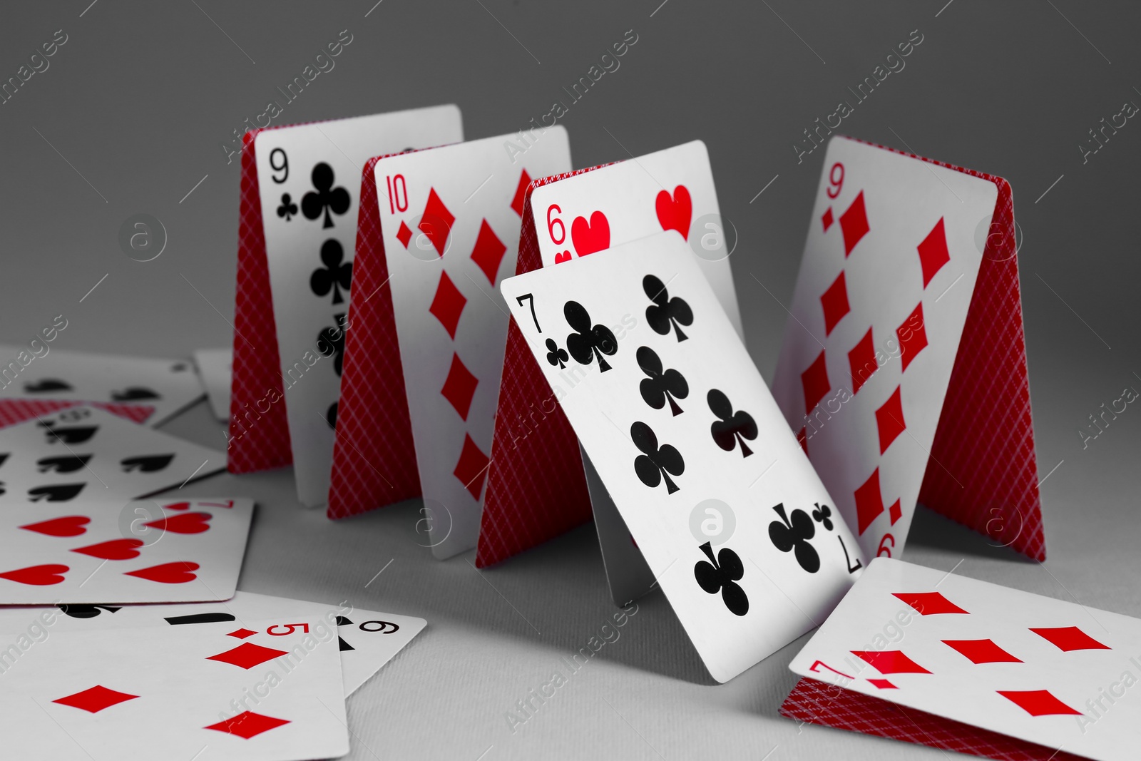 Photo of Collapsed house of playing cards on grey background, closeup