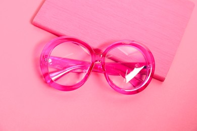 Photo of Stylish bright glasses and notebook on pink background, top view