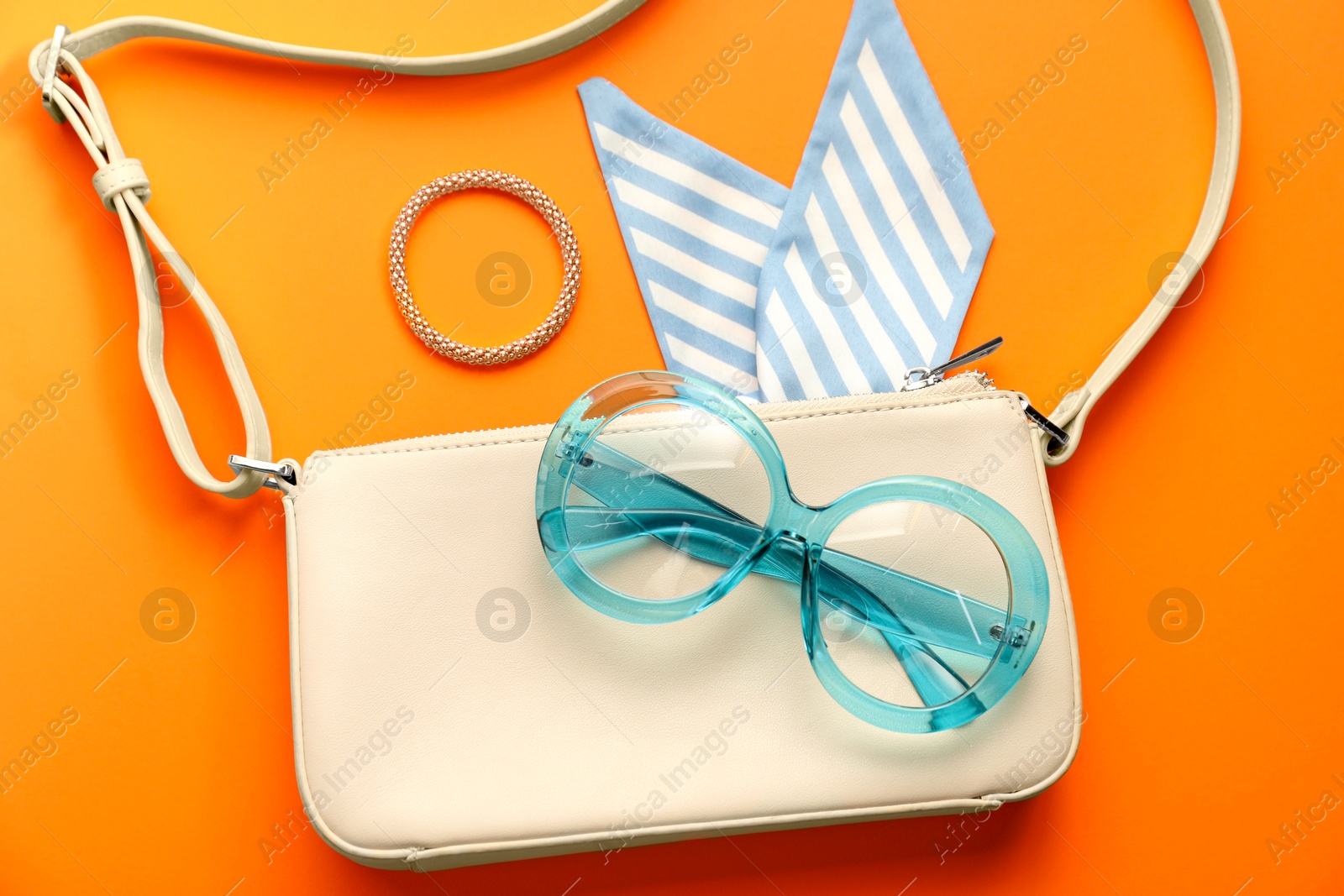 Photo of Stylish light blue glasses and other accessories on orange background, flat lay