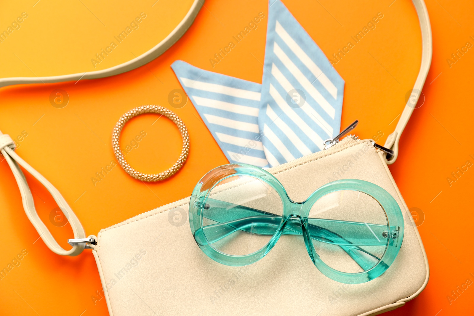 Photo of Stylish light blue glasses and other accessories on orange background, above view