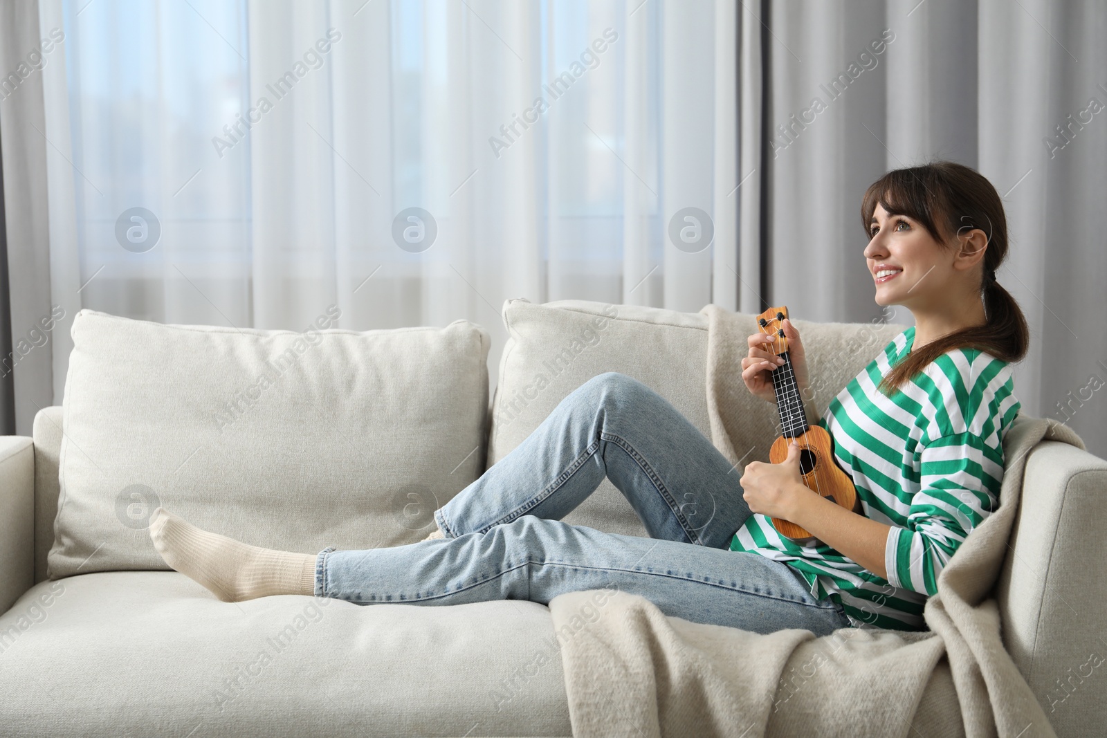 Photo of Happy woman playing ukulele on sofa at home