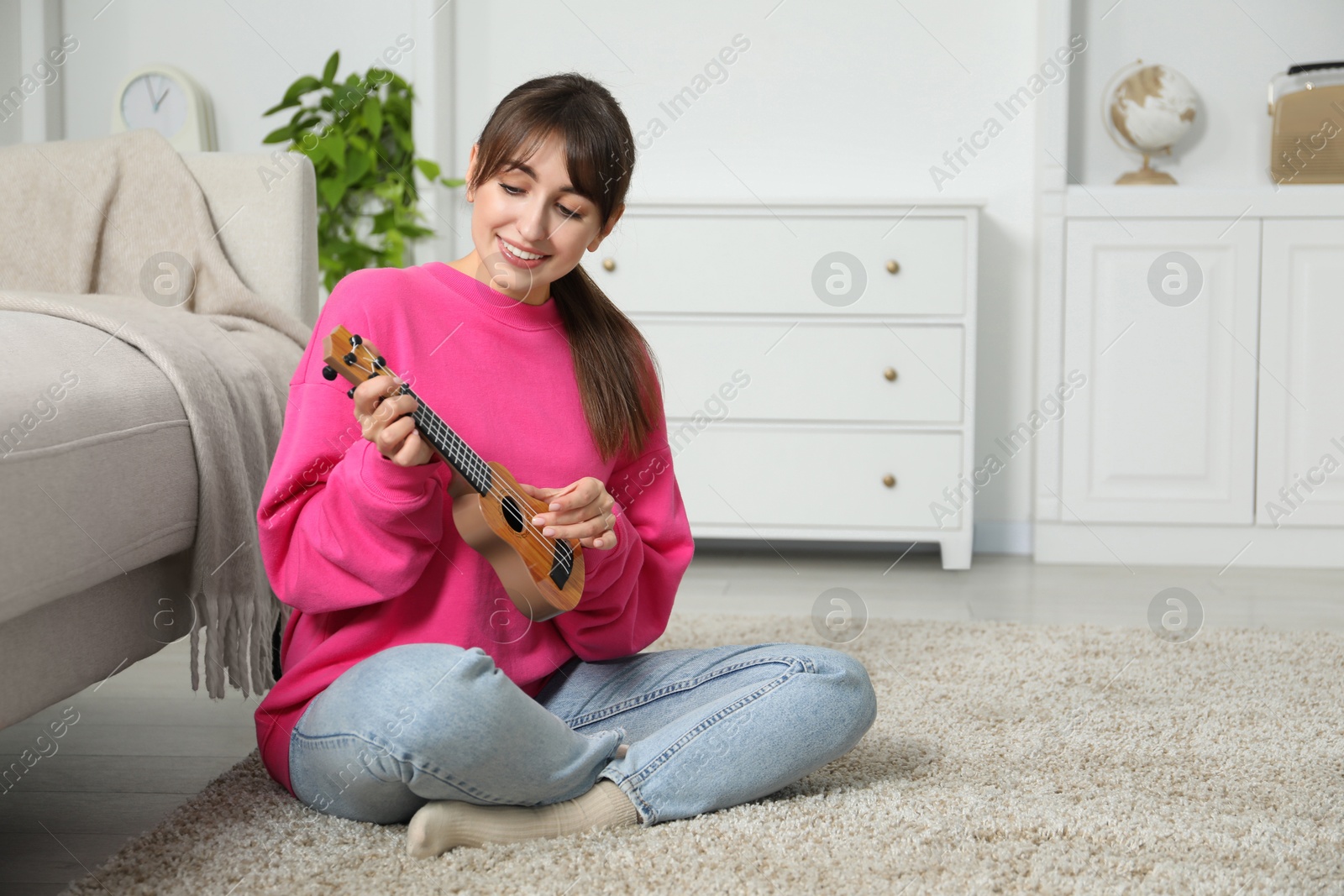 Photo of Happy woman playing ukulele on floor at home, space for text