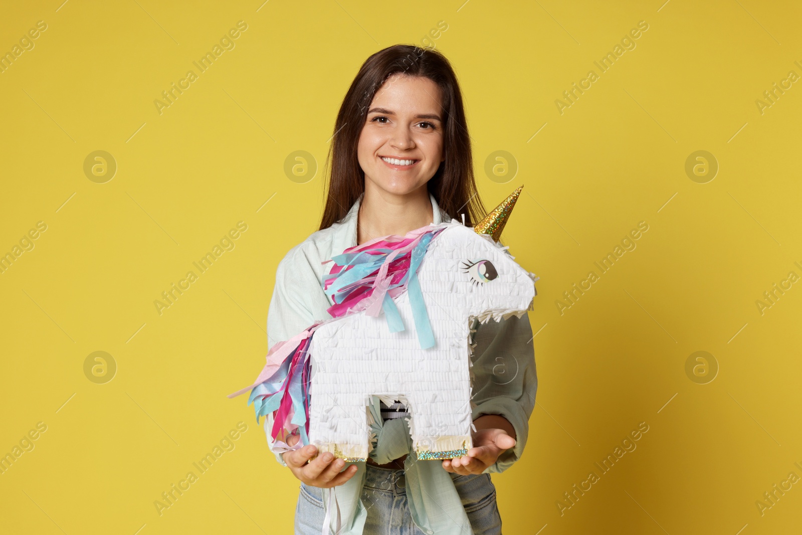 Photo of Happy woman with unicorn shaped pinata on yellow background