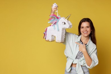 Photo of Happy woman with unicorn shaped pinata on yellow background, space for text