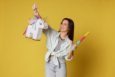 Photo of Happy woman with unicorn shaped pinata and stick on yellow background