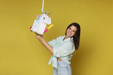 Photo of Happy woman hitting unicorn shaped pinata with stick on yellow background