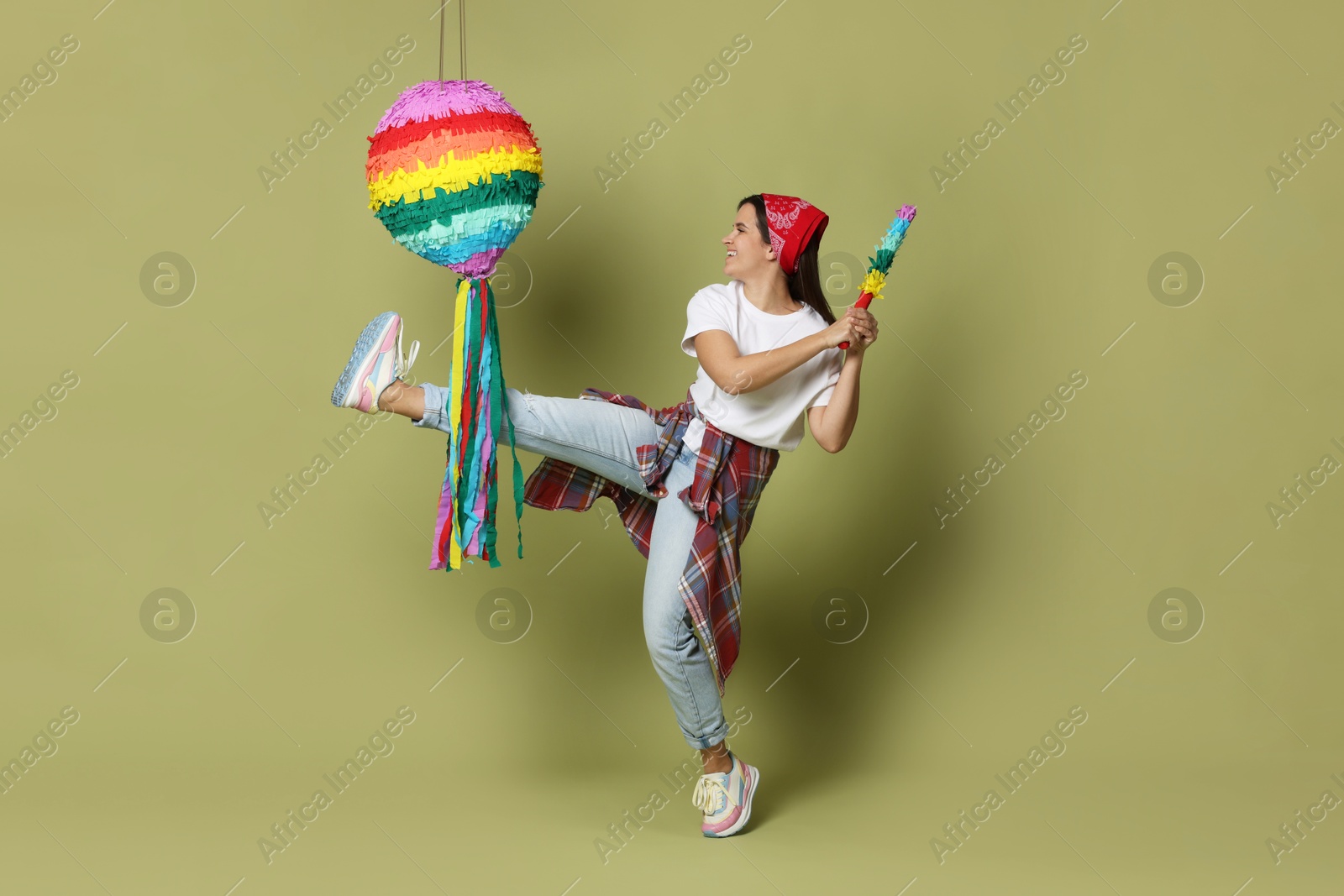 Photo of Happy woman hitting colorful pinata with stick on green background