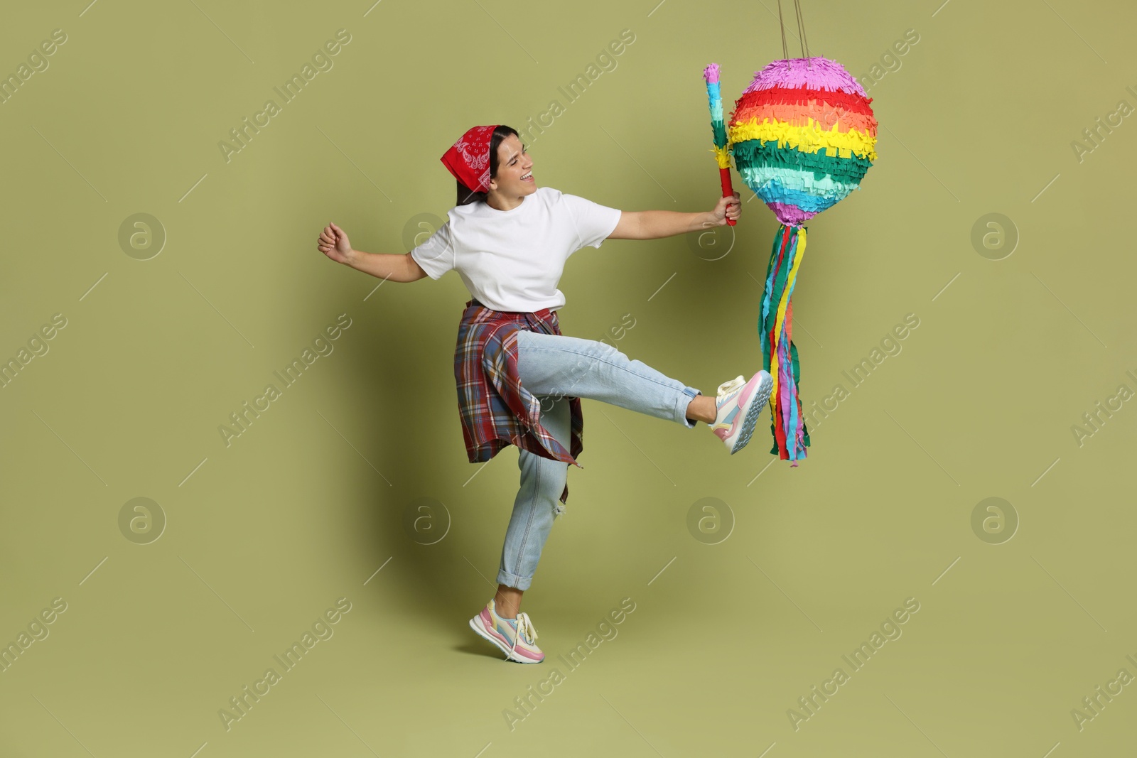 Photo of Happy woman hitting colorful pinata with stick on green background