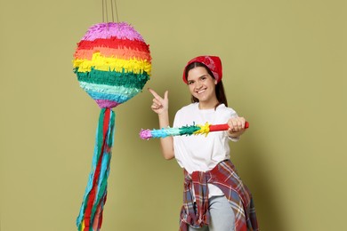 Photo of Happy woman with colorful pinata and stick on green background