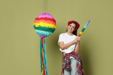 Photo of Happy woman with colorful pinata and stick on green background