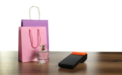 Photo of Payment terminal, perfume and shopping bags on wooden table against white background