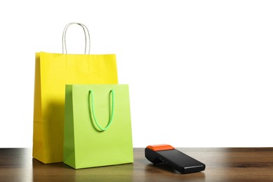 Photo of Payment terminal and shopping bags on wooden table against white background