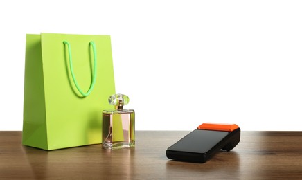 Photo of Payment terminal, perfume and shopping bag on wooden table against white background