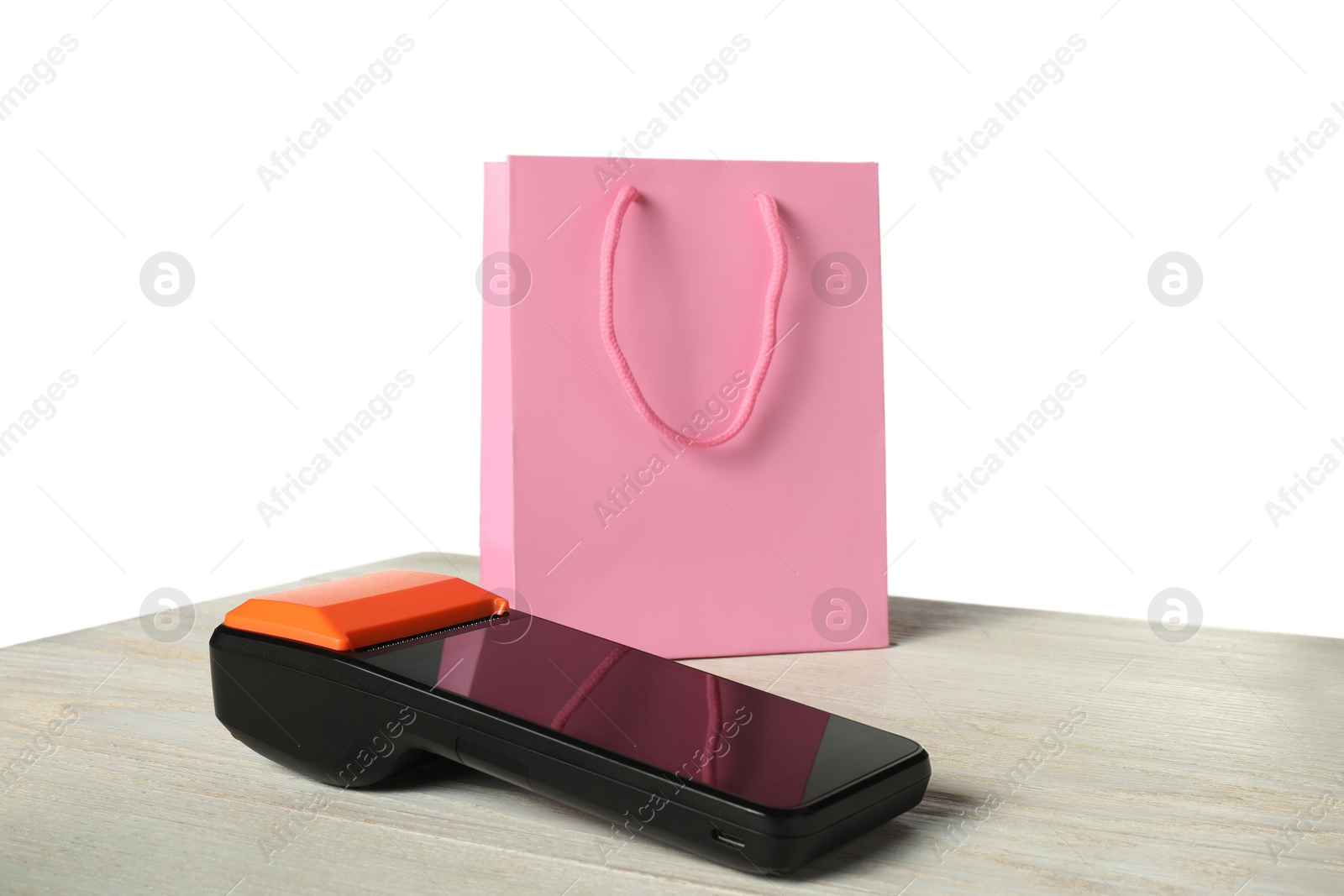 Photo of Payment terminal and shopping bag on wooden table against white background