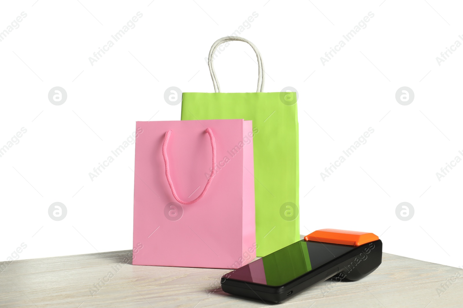 Photo of Payment terminal and shopping bags on wooden table against white background