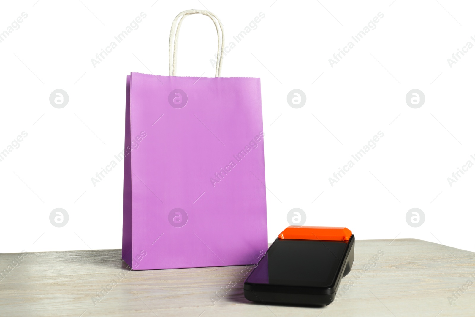 Photo of Payment terminal and shopping bag on wooden table against white background